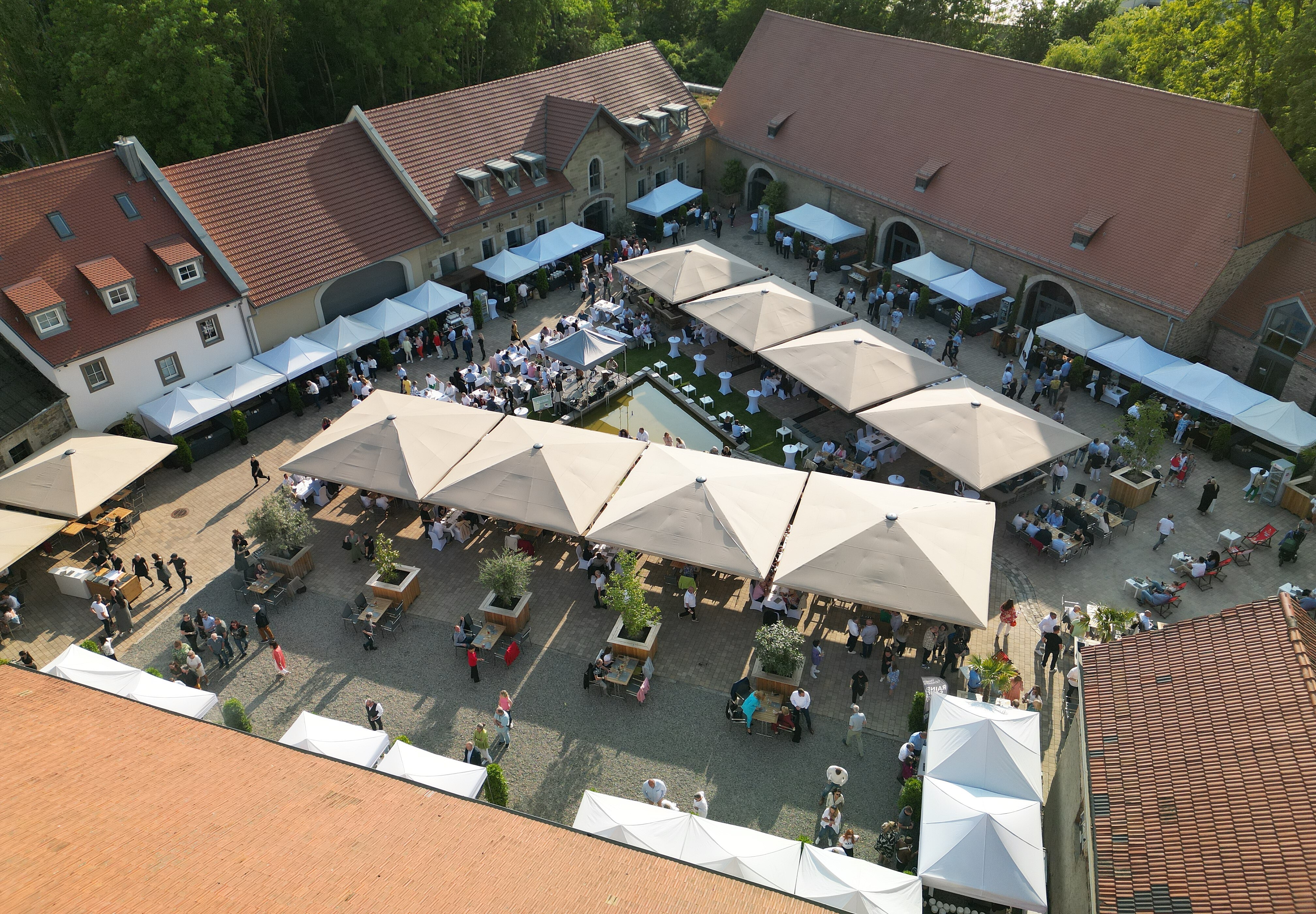 Innen & außen Viele Gäste im großen Außenbereich der Eventlocation Gut Wöllried Würzburg bei einem sommerlichen Firmenevent