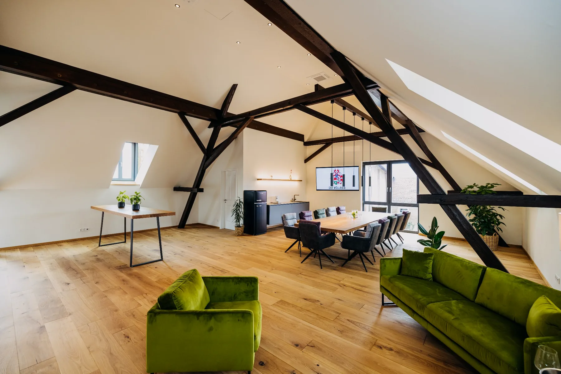 Lichtdurchflutetes Loft der Brennerei auf Gut Wöllried mit grünen Loungesofas, Konferenztisch und historischem Dachgebälk