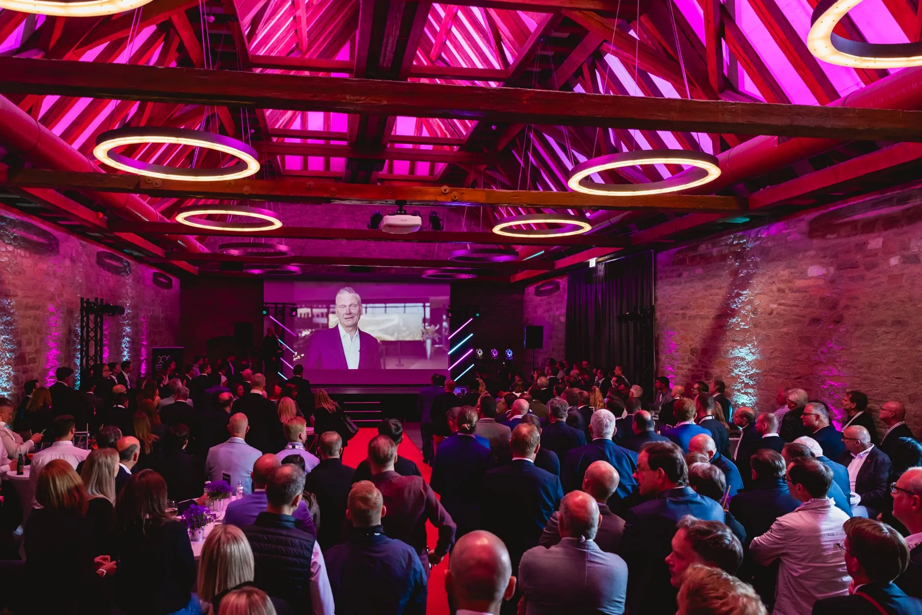 Gut besuchte Firmenveranstaltung in der Festscheune auf Gut Wöllried mit großer Leinwand und pinkfarbener Bühnenbeleuchtung