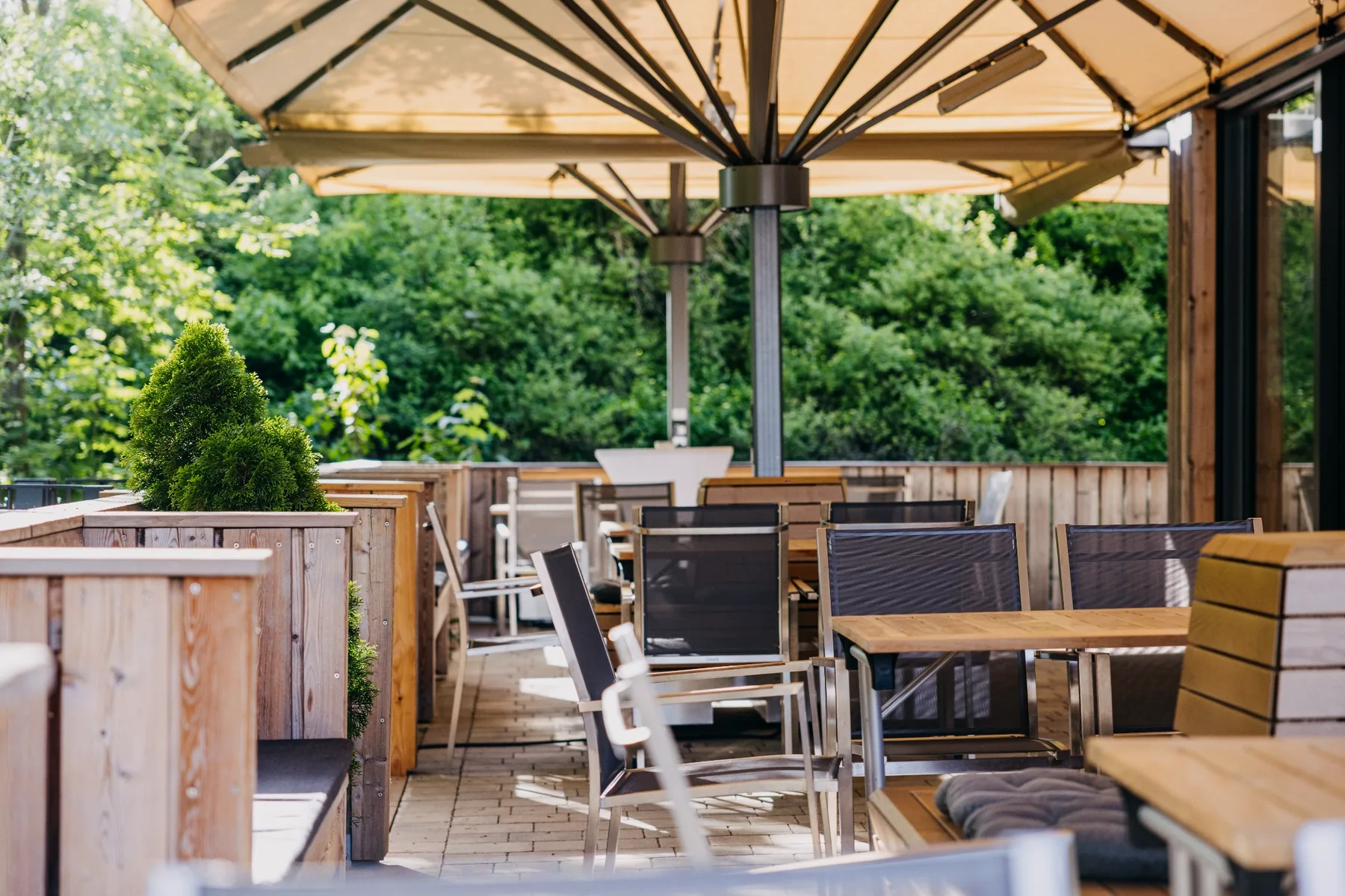 Überdachte Terrasse am Ulrichsaal auf Gut Wöllried mit Holzbänken, Sitzgruppen und Blick ins Grüne
