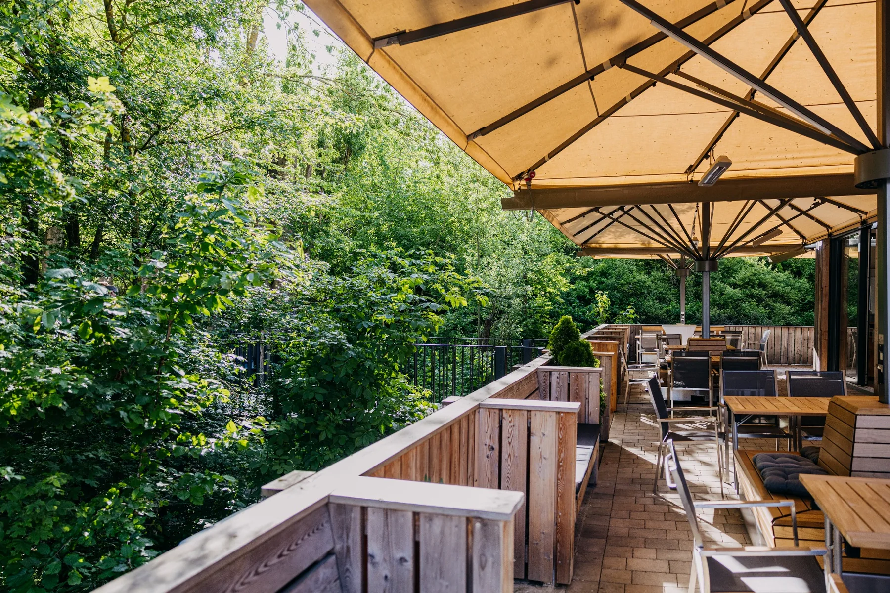 Großzügige Terrasse des Ulrichsaals auf Gut Wöllried mit Sonnenschirmen und Sitzgelegenheiten direkt am Waldrand