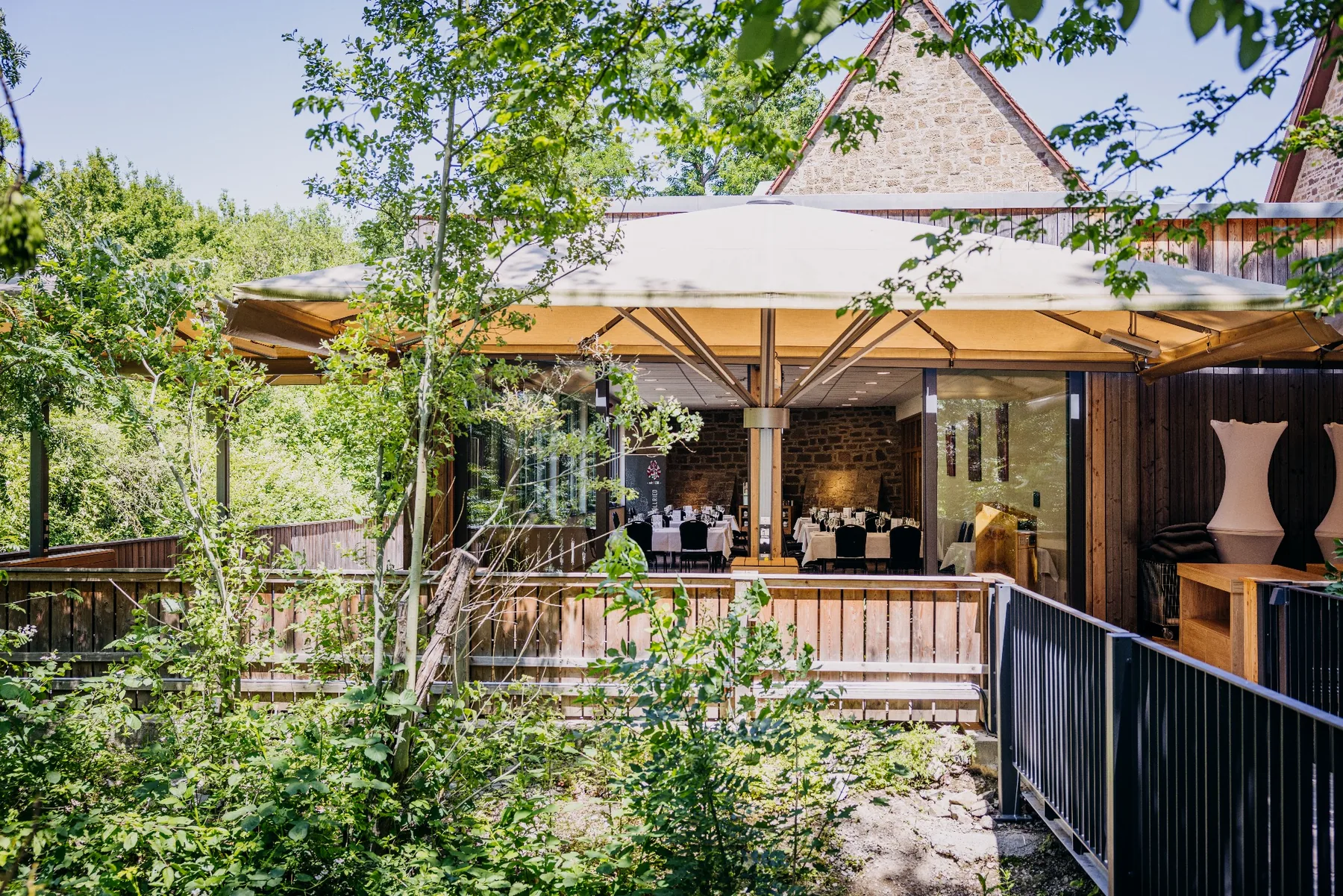 Außenansicht des Ulrichsaals auf Gut Wöllried mit großer überdachter Terrasse, Sonnenschirmen und angrenzendem Grün