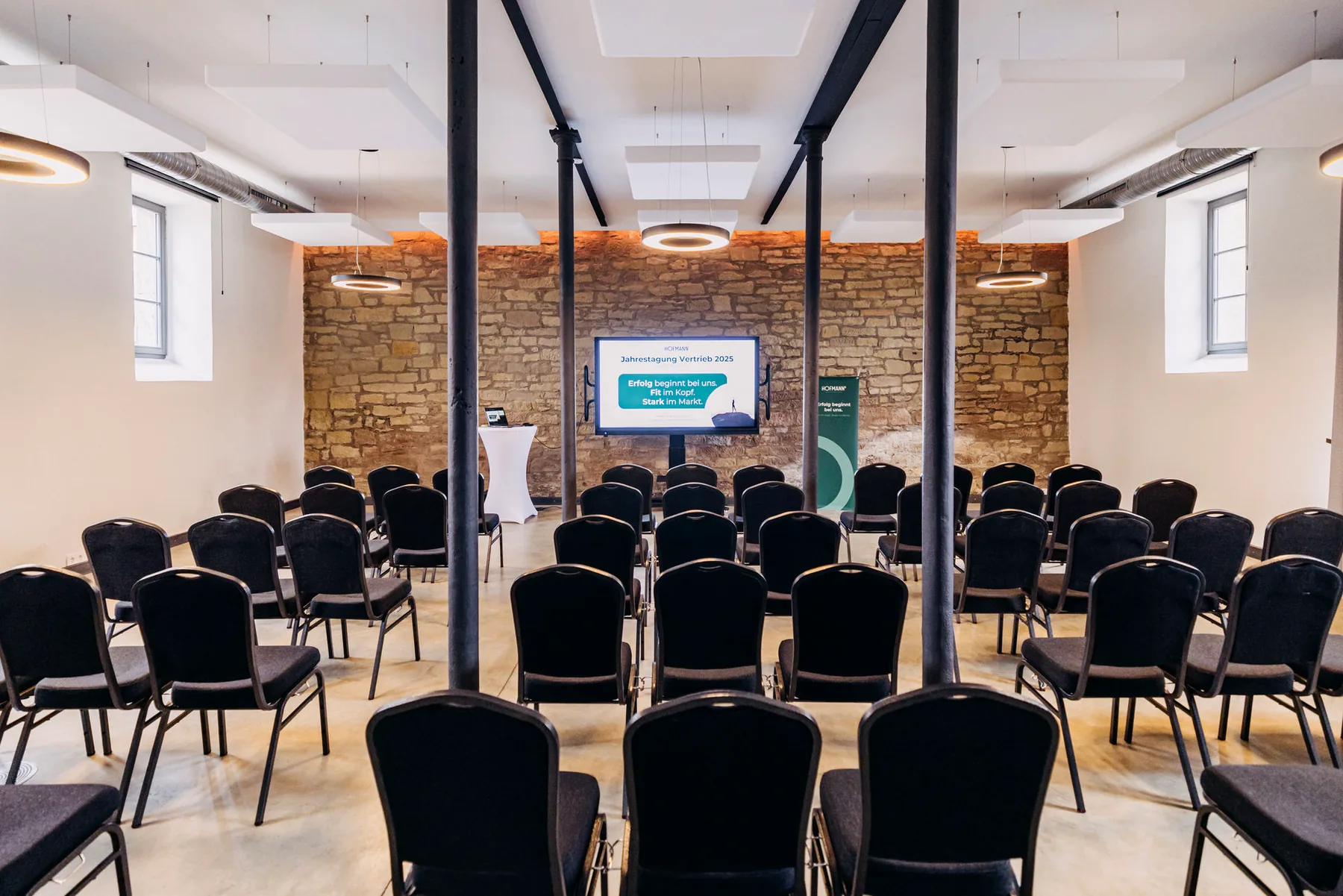 Konferenzraum im Alten Speicher auf Gut Wöllried mit Reihenbestuhlung, Präsentationsbildschirm und historischer Natursteinwand