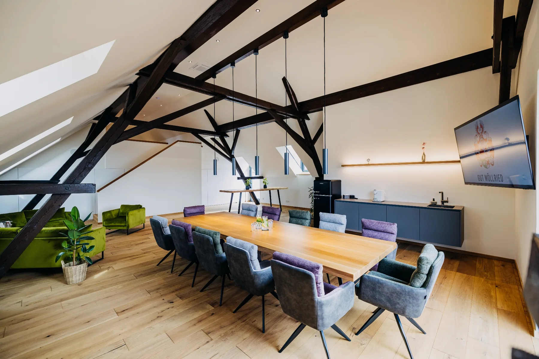 Meetingbereich im Loft der Brennerei auf Gut Wöllried mit großem Holztisch, Bildschirm und angrenzender Lounge
