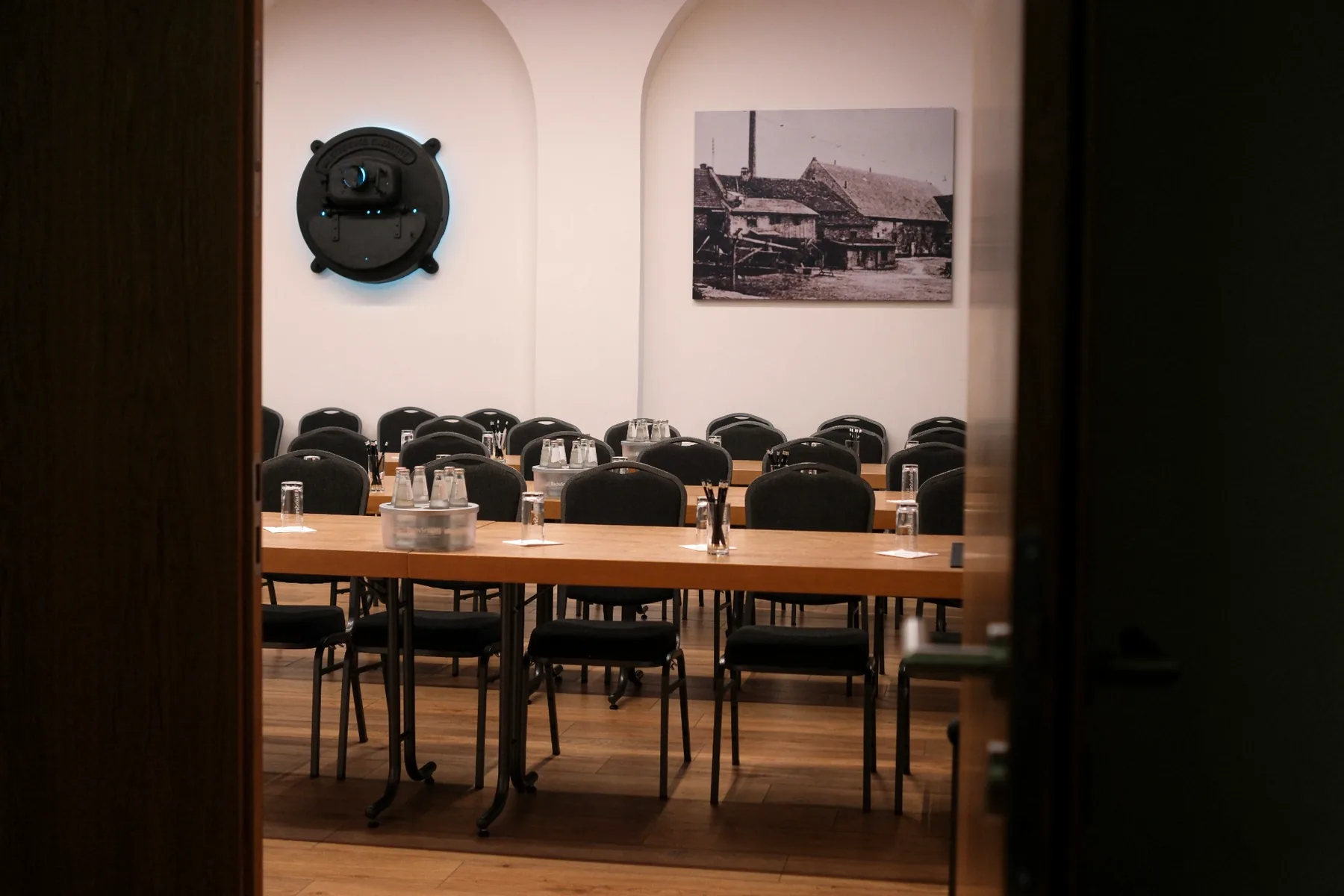 Vorbereiteter Konferenzraum in der Brennerei auf Gut Wöllried mit Tischbestuhlung, Tagungsgetränken und historischem Wandbild