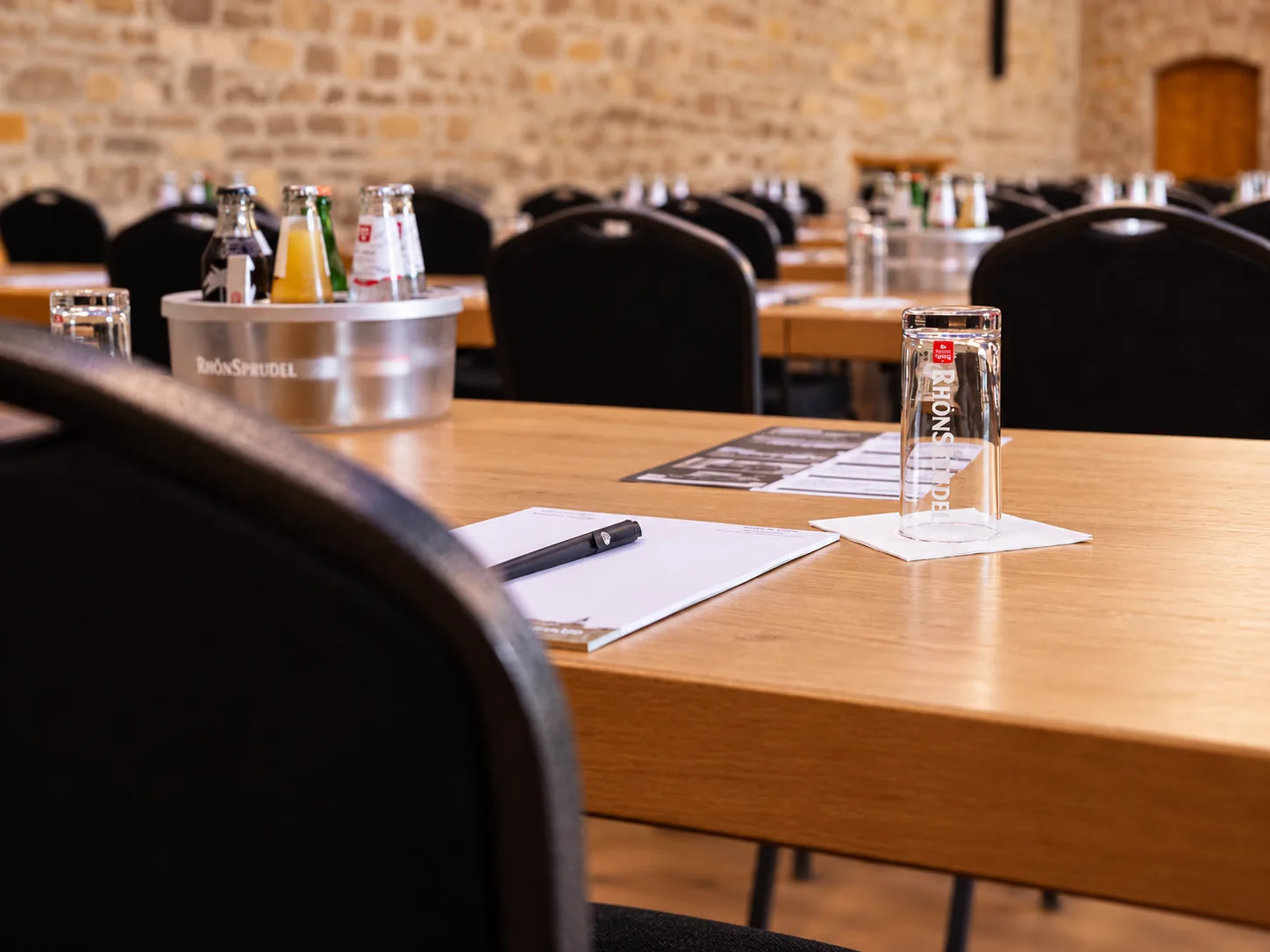 Gedeckter Konferenztisch in der Festscheune auf Gut Wöllried mit Schreibunterlagen, Getränken und Wassergläsern